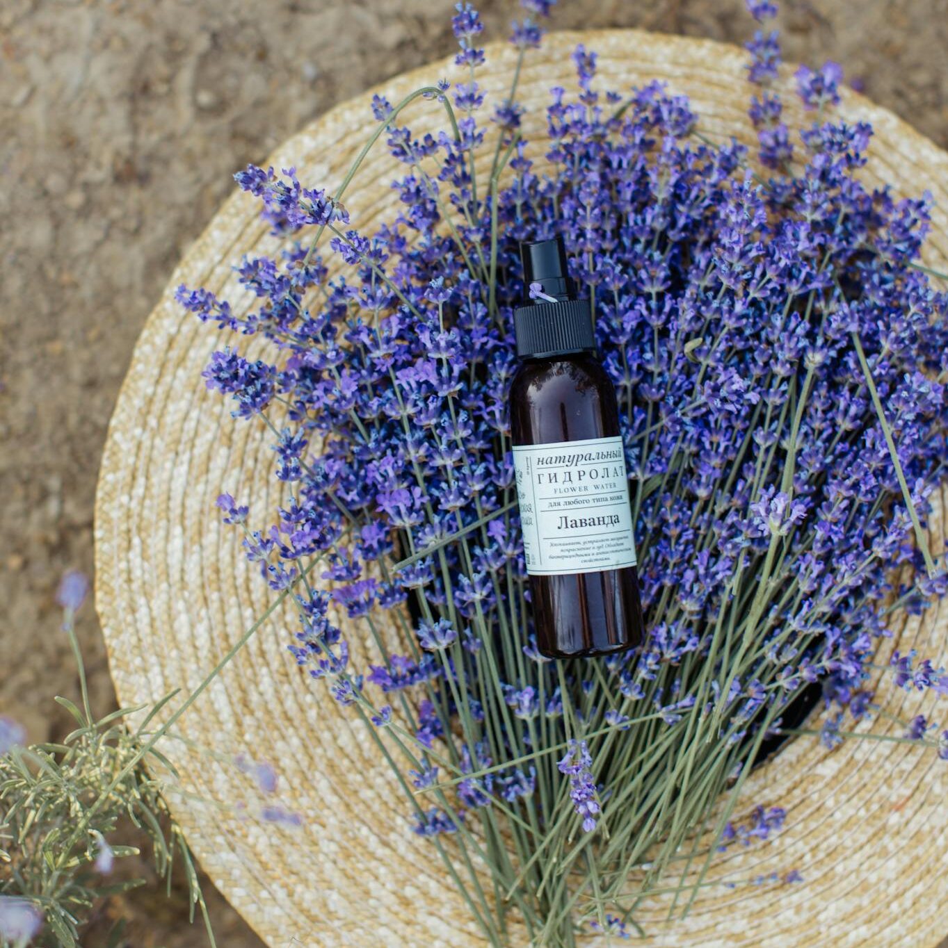 A bottle of lavender perfume resting on a straw hat with fresh lavender flowers.