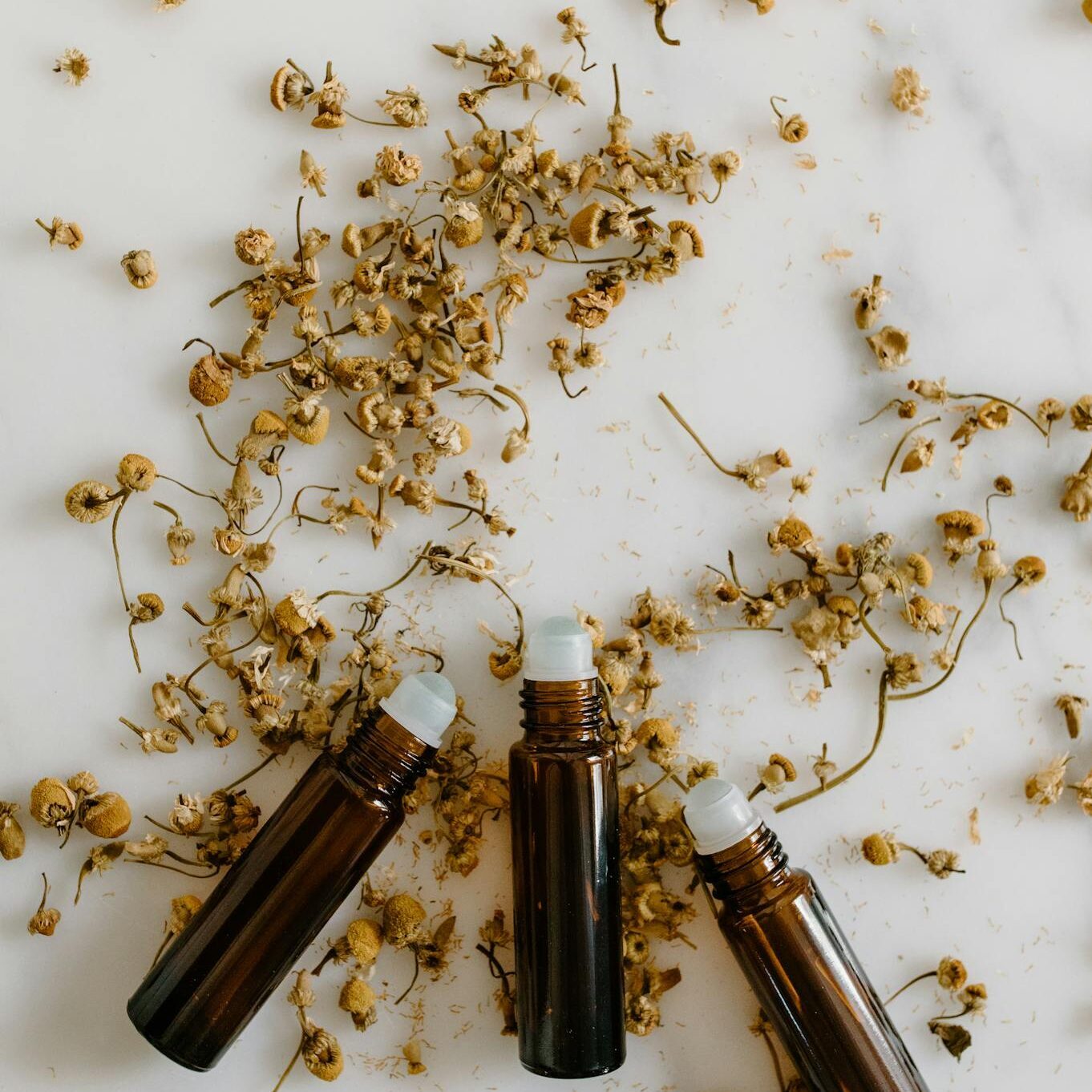 Top view of roll-on bottles surrounded by dried herbal flowers, perfect for alternative medicine concepts.